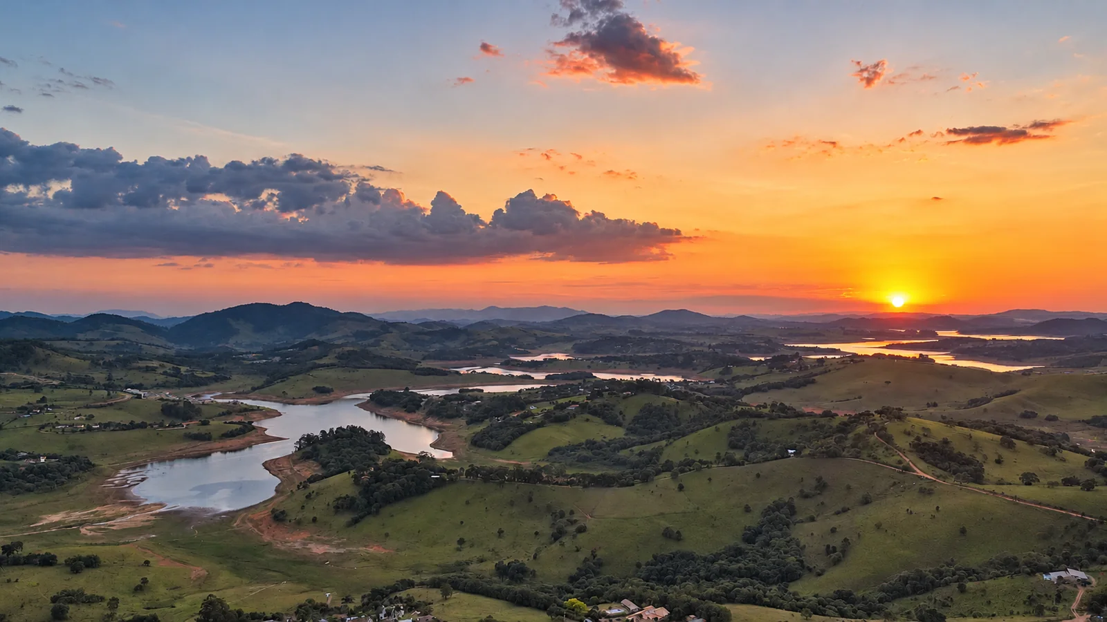 Paisagem aérea da região ao pôr do sol, com montanhas e represa